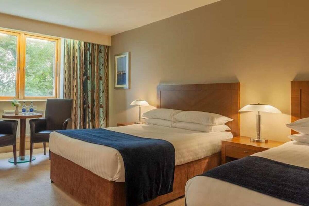 A hotel room with two beds, a desk, a chair, and a window with curtains.