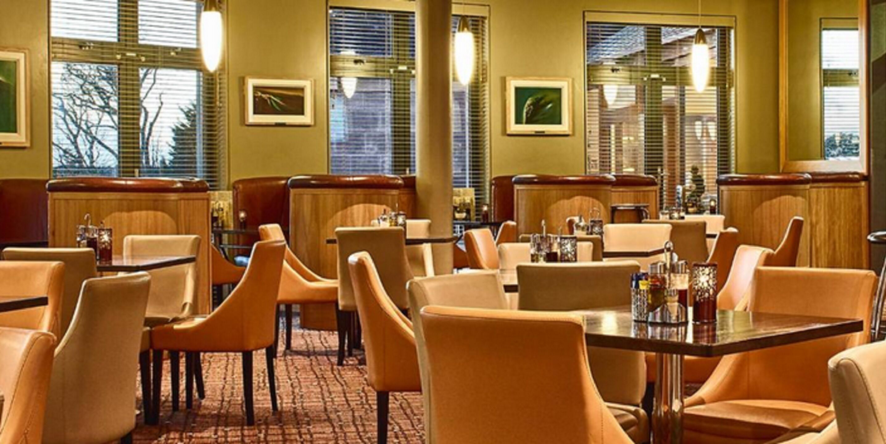 A restaurant with booths and tables, large windows with blinds, and framed pictures on the walls.
