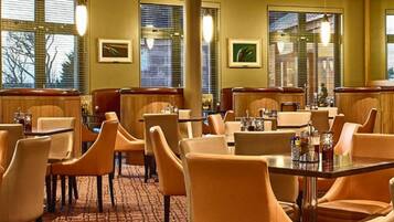 A restaurant with booths and tables, large windows with blinds, and framed pictures on the walls.
