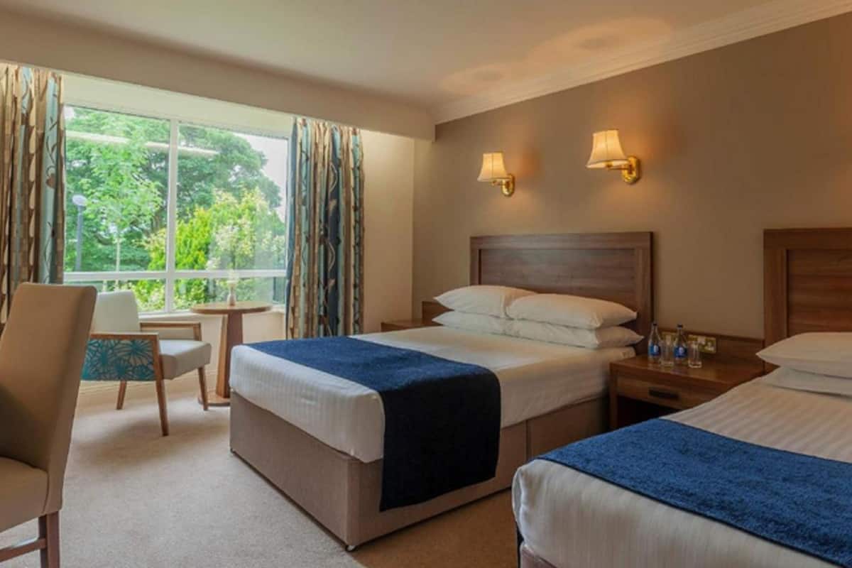 A hotel room with two beds, a desk, a chair, and a window with curtains.