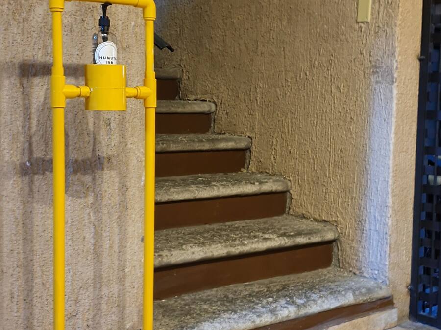 Une rambarde jaune à côté d’un escalier, un tapis noir au bas de l’escalier et un panneau indiquant les noms des pièces et les numéros des étages.