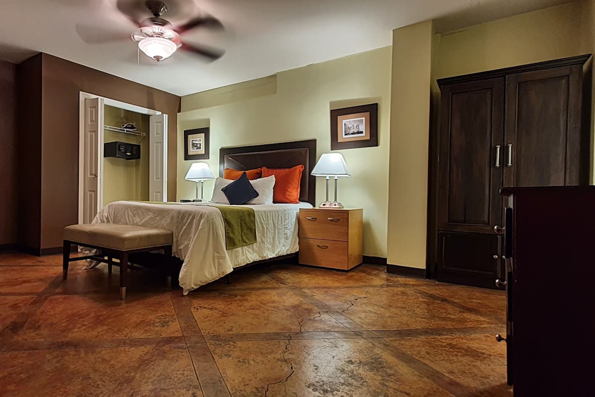 Una camera da letto con un letto, comodini, una sedia, un armadio e una ventola a soffitto.