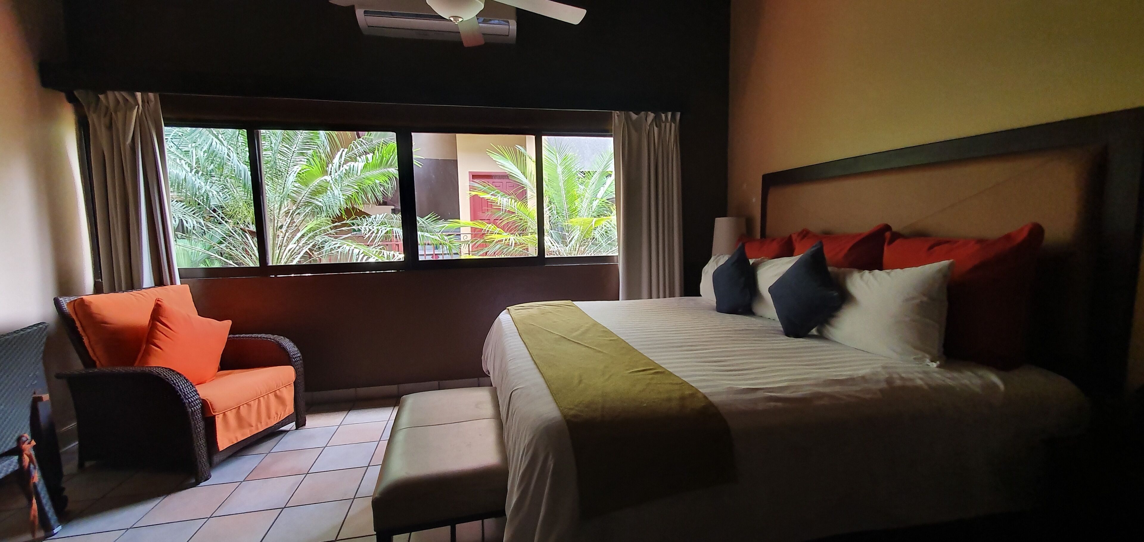 A hotel room with a bed, a sofa, and a window with a view of greenery.