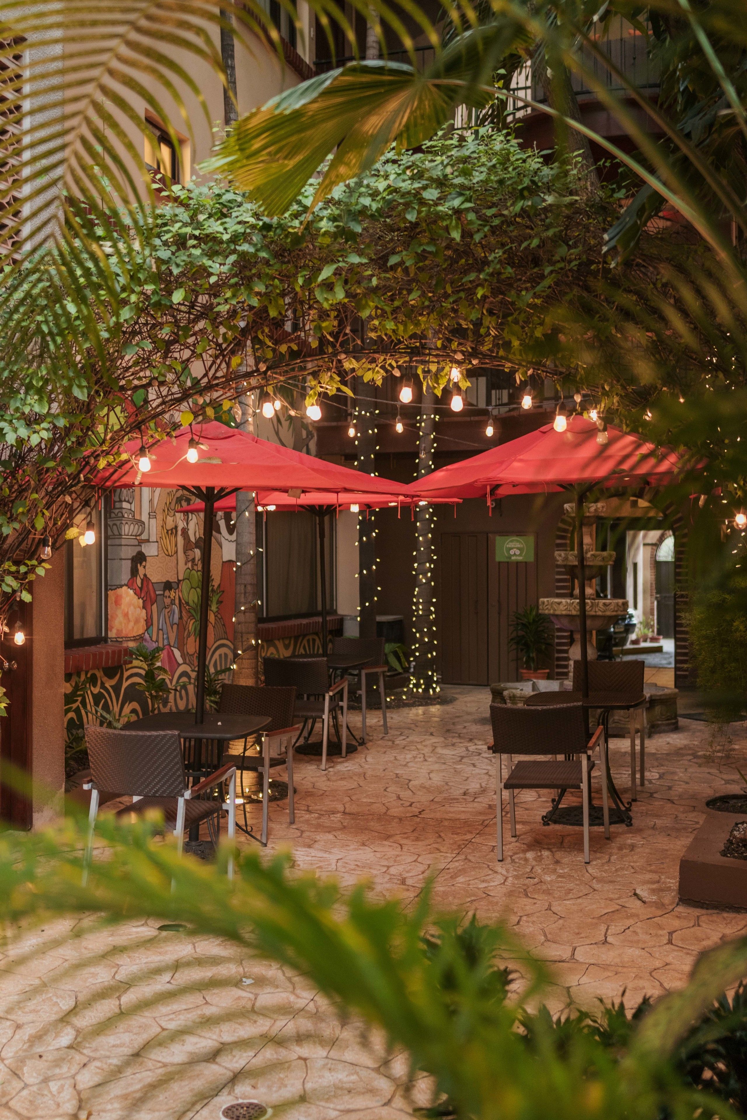 Un patio al aire libre con sombrillas rojas, muebles de mimbre e iluminación con luces colgantes.