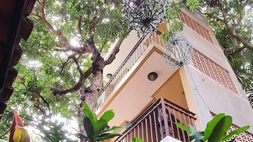 A building with a balcony, surrounded by lush greenery and potted plants.