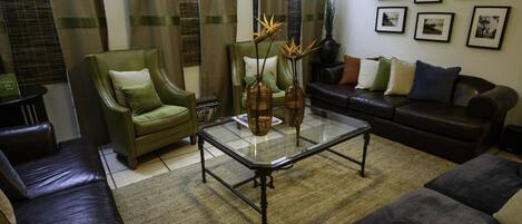 A living room with a glass coffee table, green armchair, and a dark leather sofa.