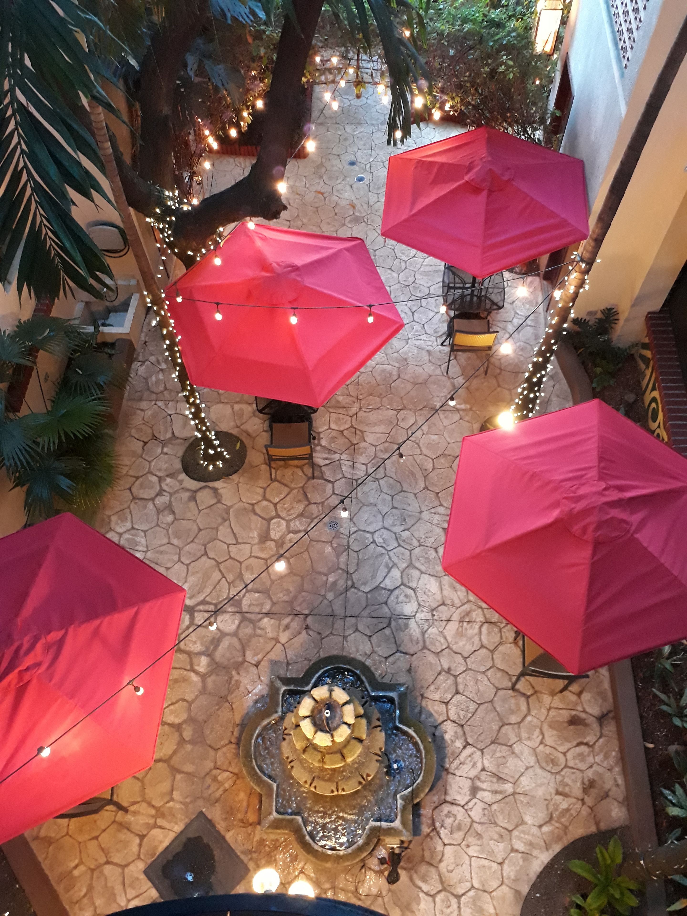 A courtyard with stone flooring, red umbrellas, and string lights.