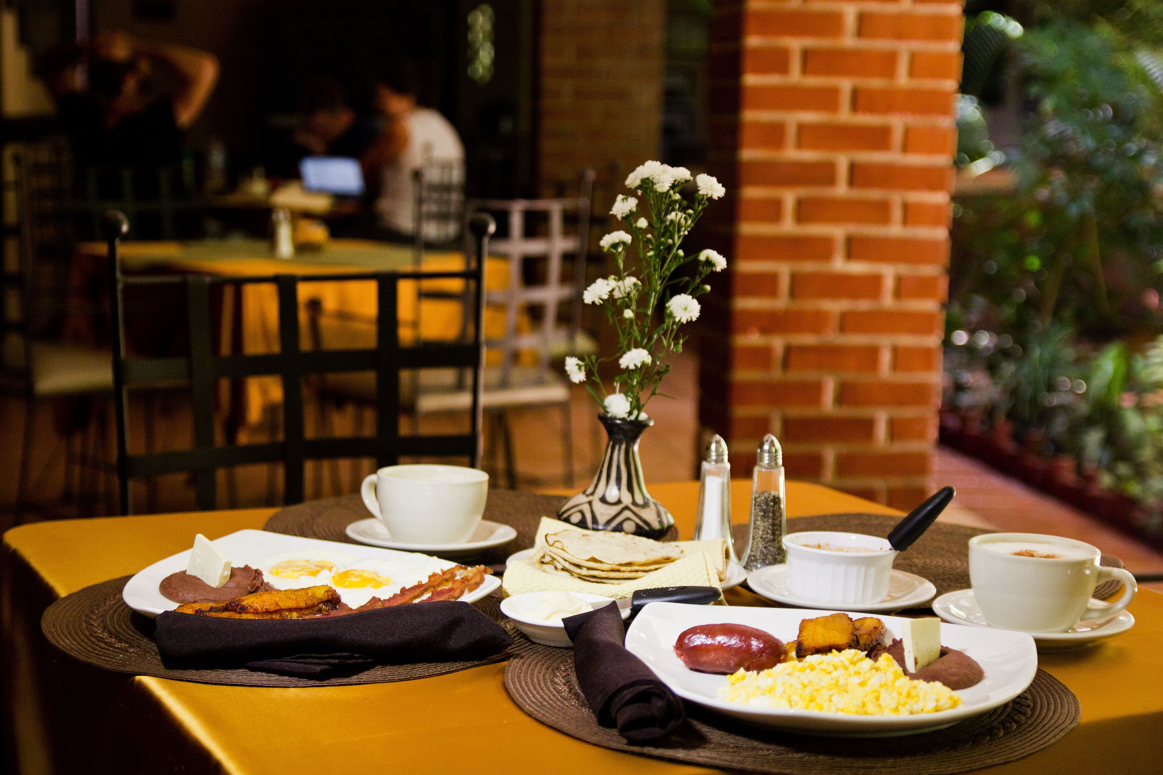 A breakfast table with plates of food, a vase of flowers, and a coffee cup.