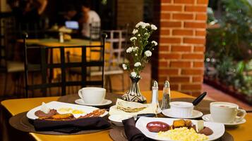 A breakfast table with plates of food, a vase of flowers, and a coffee cup.