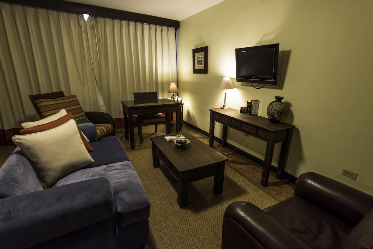 Una camera d'albergo con un divano, un tavolino, una televisione e una lampada.