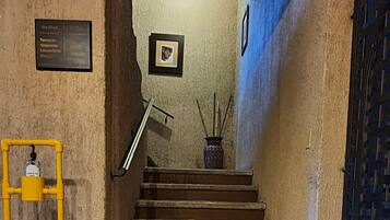 A staircase with a yellow handrail, a black mat at the bottom, and a wall-mounted sign listing room types.