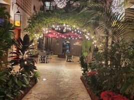 Un patio al aire libre con suelo de piedra, mesas, sillas y plantas en macetas.