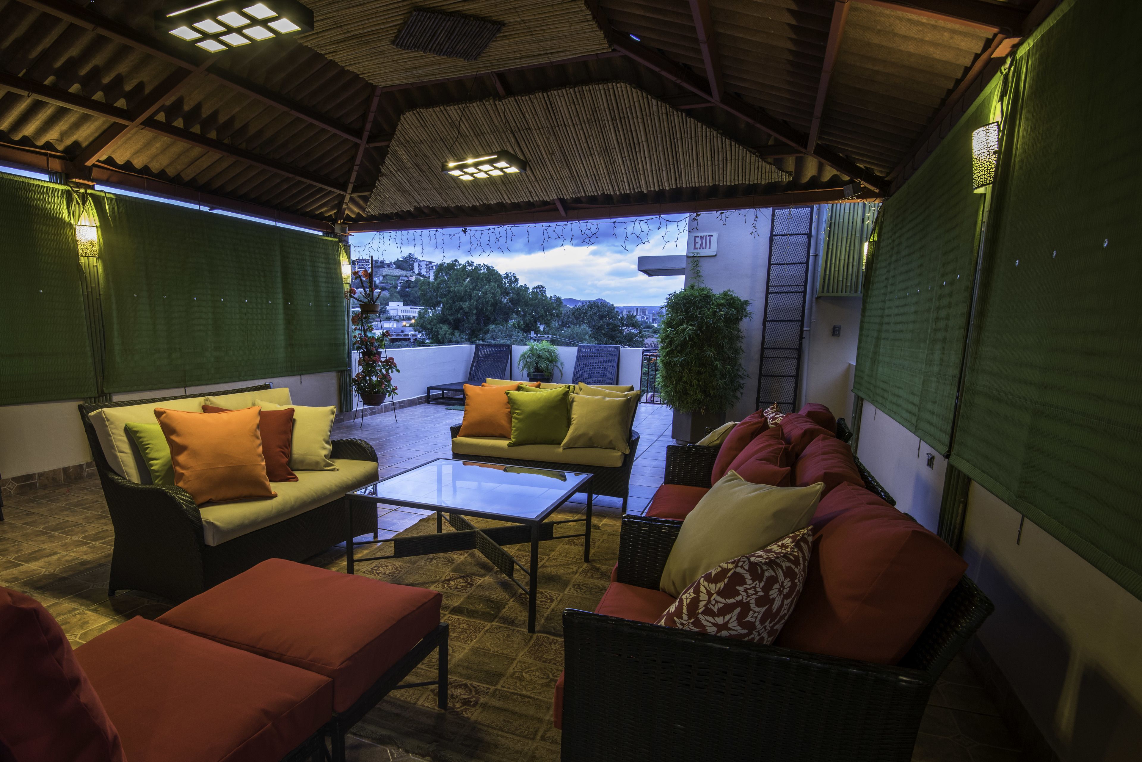 En udendørs patio med overdækket siddeområde, inklusive en sofa og stole, et sofabord og plantekrukker.