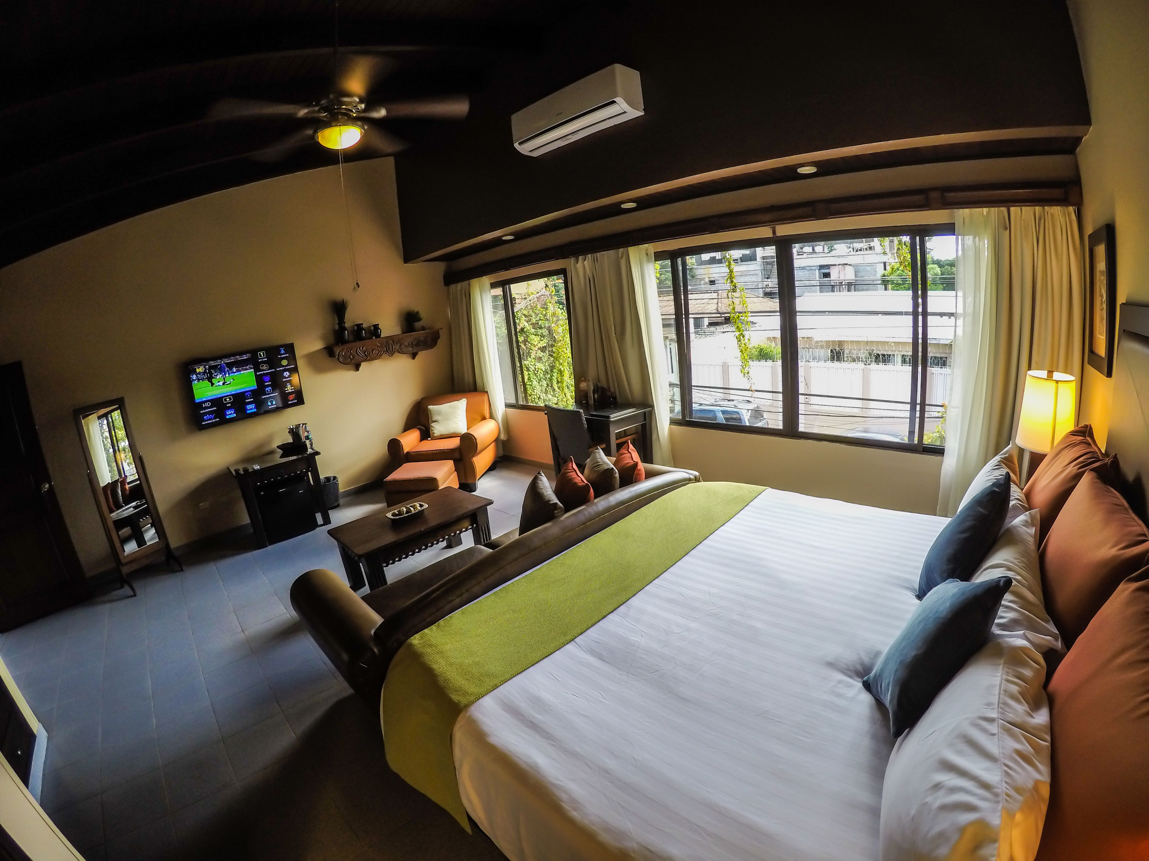 Habitación de hotel con cama, escritorio, silla, televisor y ventana con vista a edificios y áreas verdes.