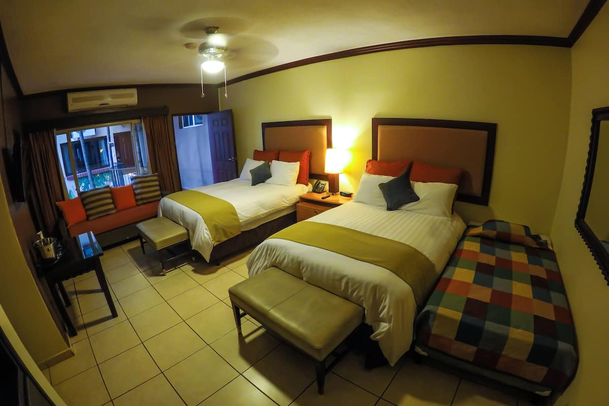 Una camera d'albergo con due letti, una poltrona letto, una scrivania e una finestra con tende.