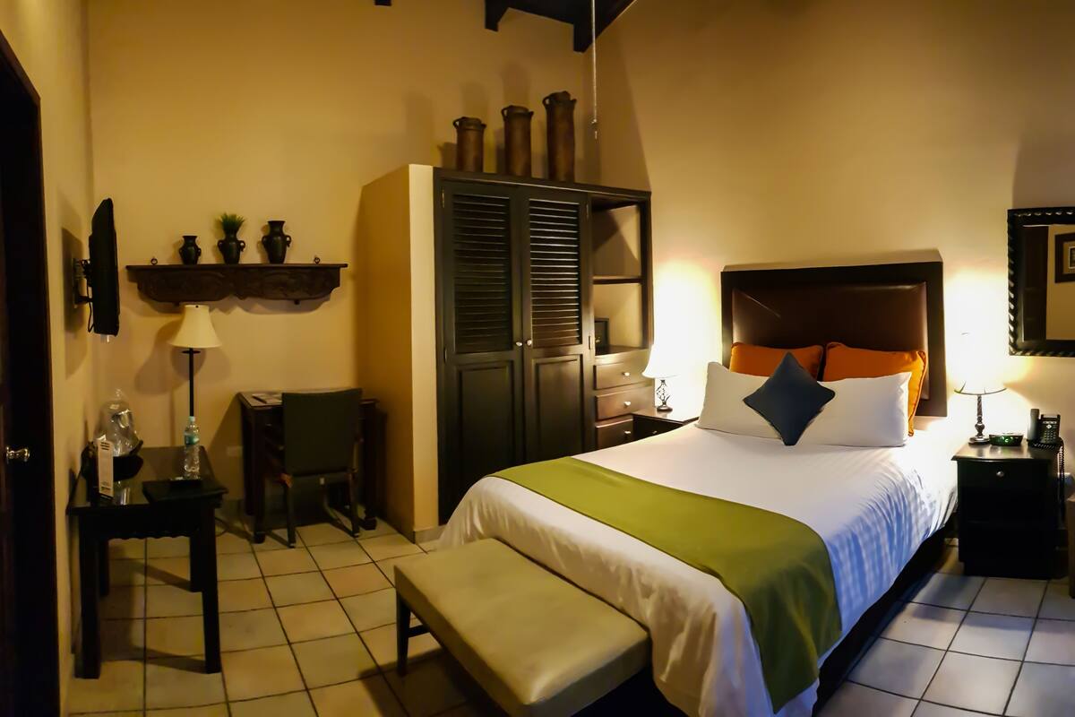 Camera d'albergo con un letto, una panca, una scrivania, una sedia, un armadio e un comodino.