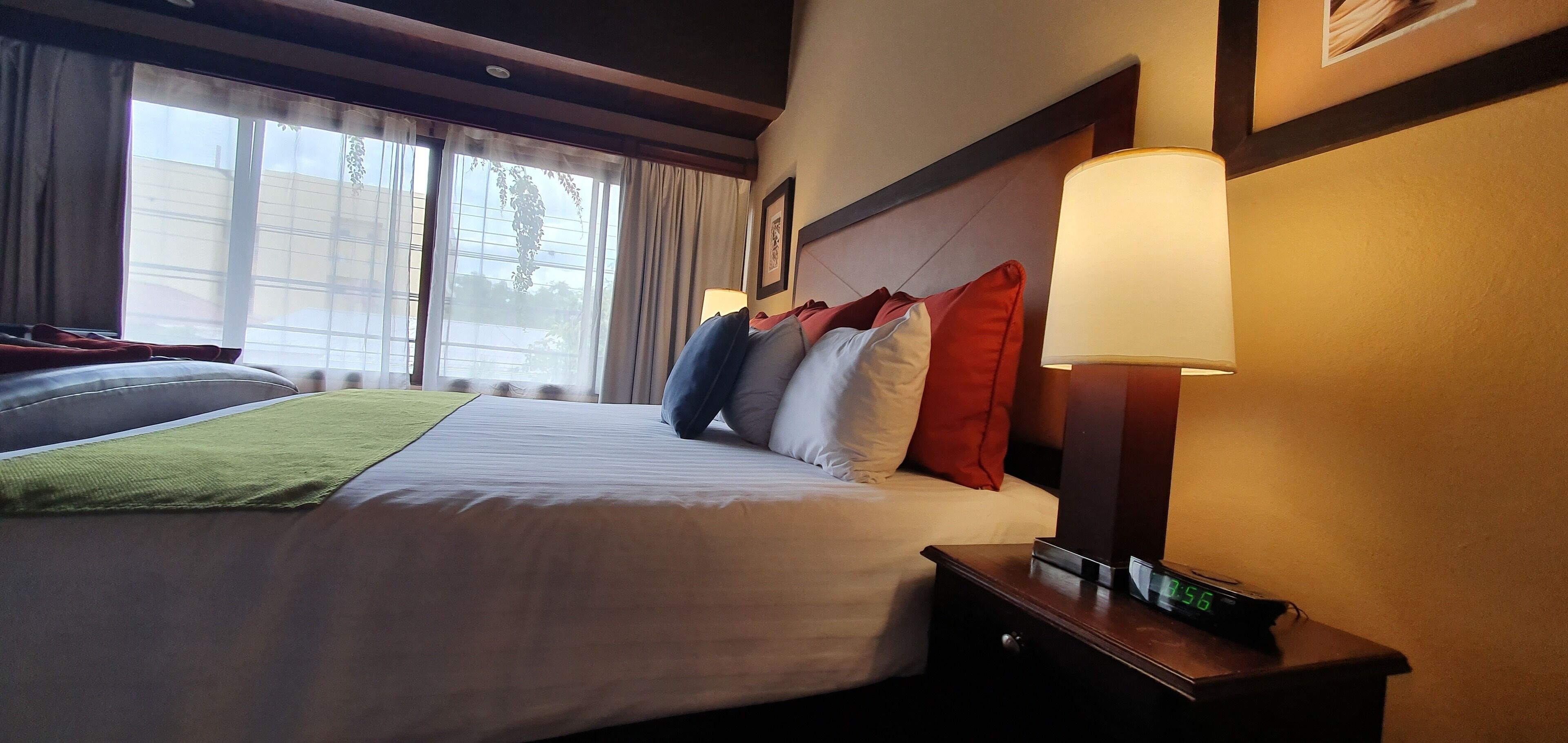 Une chambre d’hôtel avec un lit bien fait, une lampe de chevet et une horloge numérique sur la table de chevet.