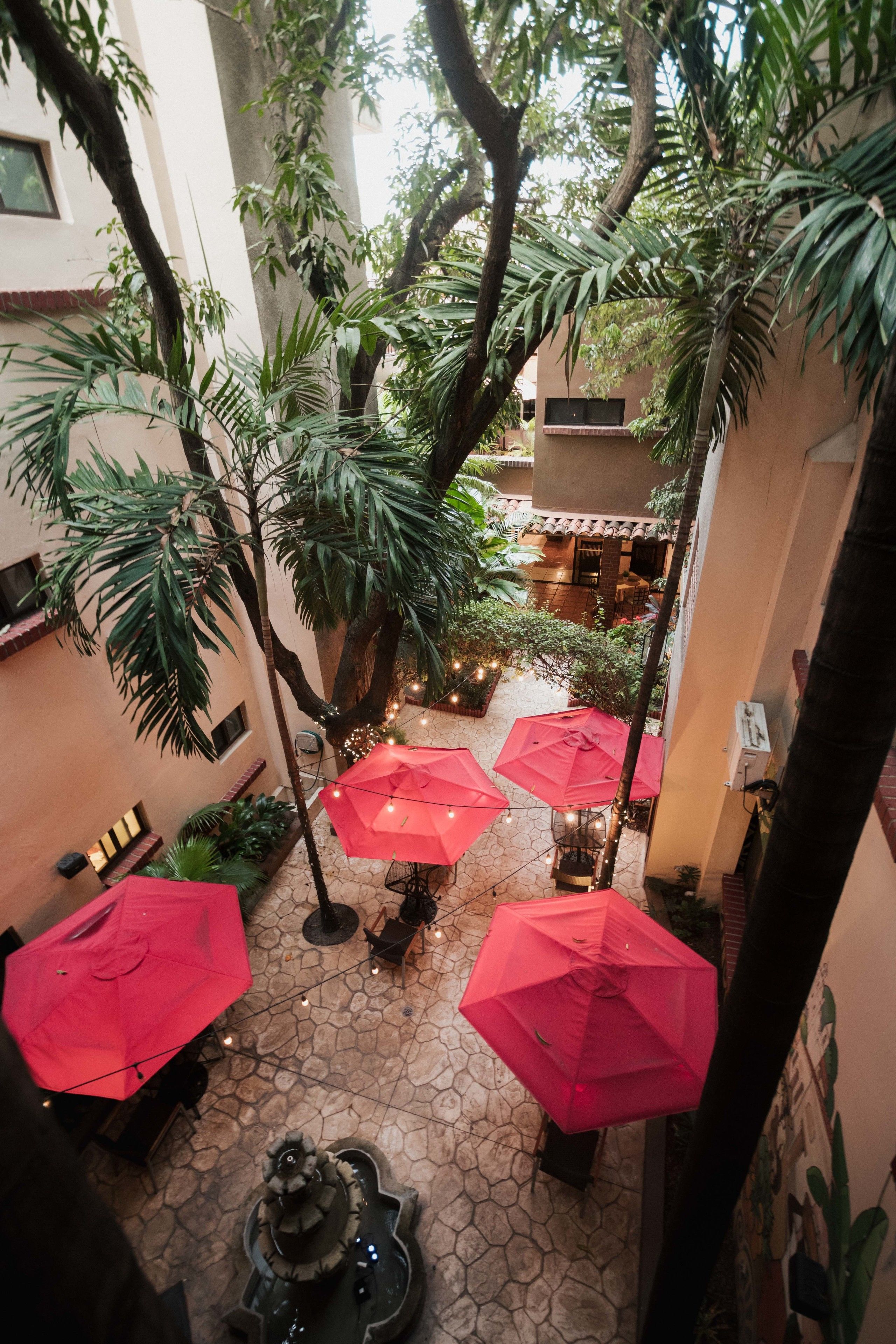 Een binnentuin met rode parasols, stenen vloer en potplanten.