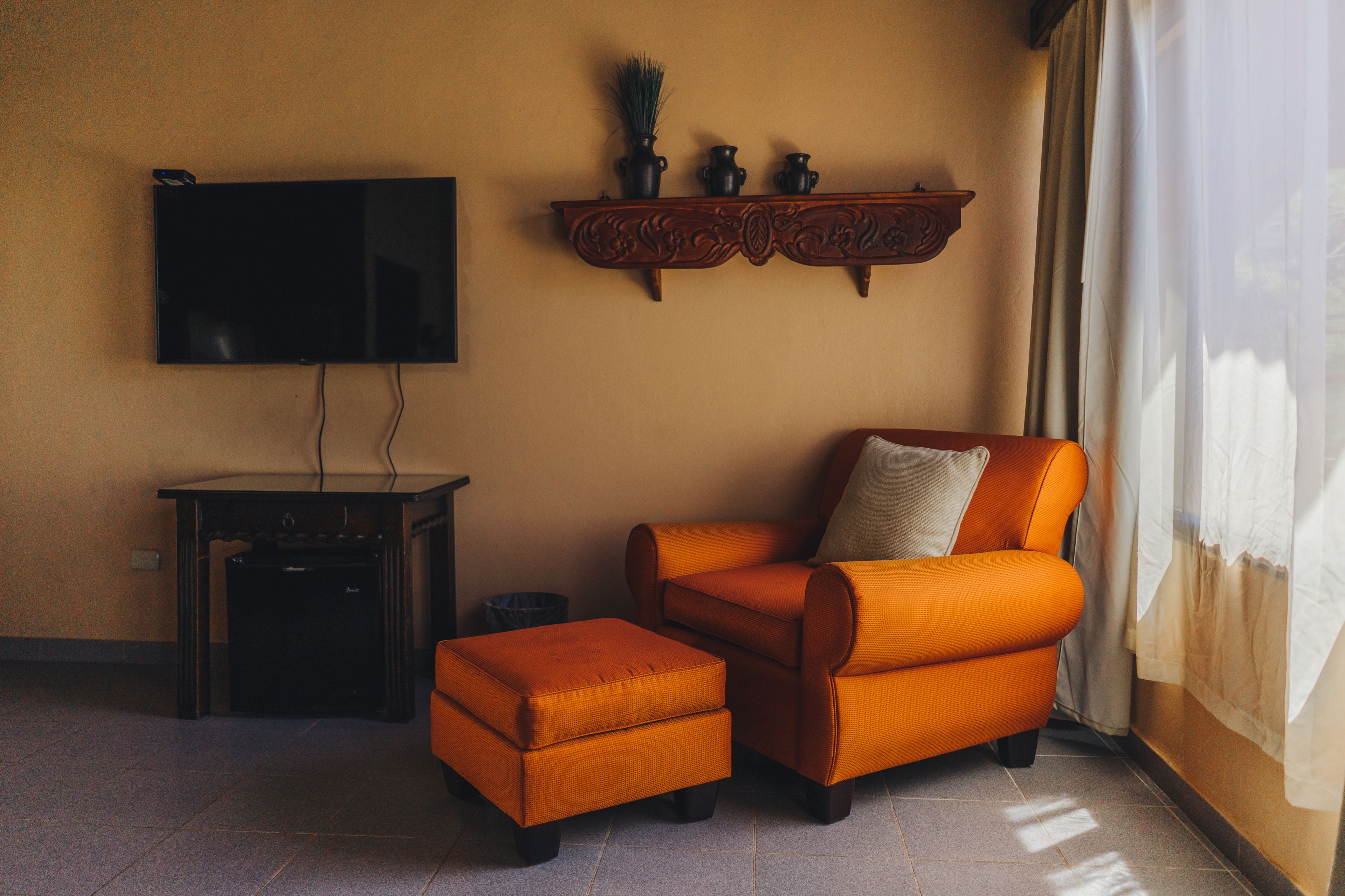 A living room with a flat-screen TV, a wooden entertainment unit, an orange armchair, and a matching ottoman.
