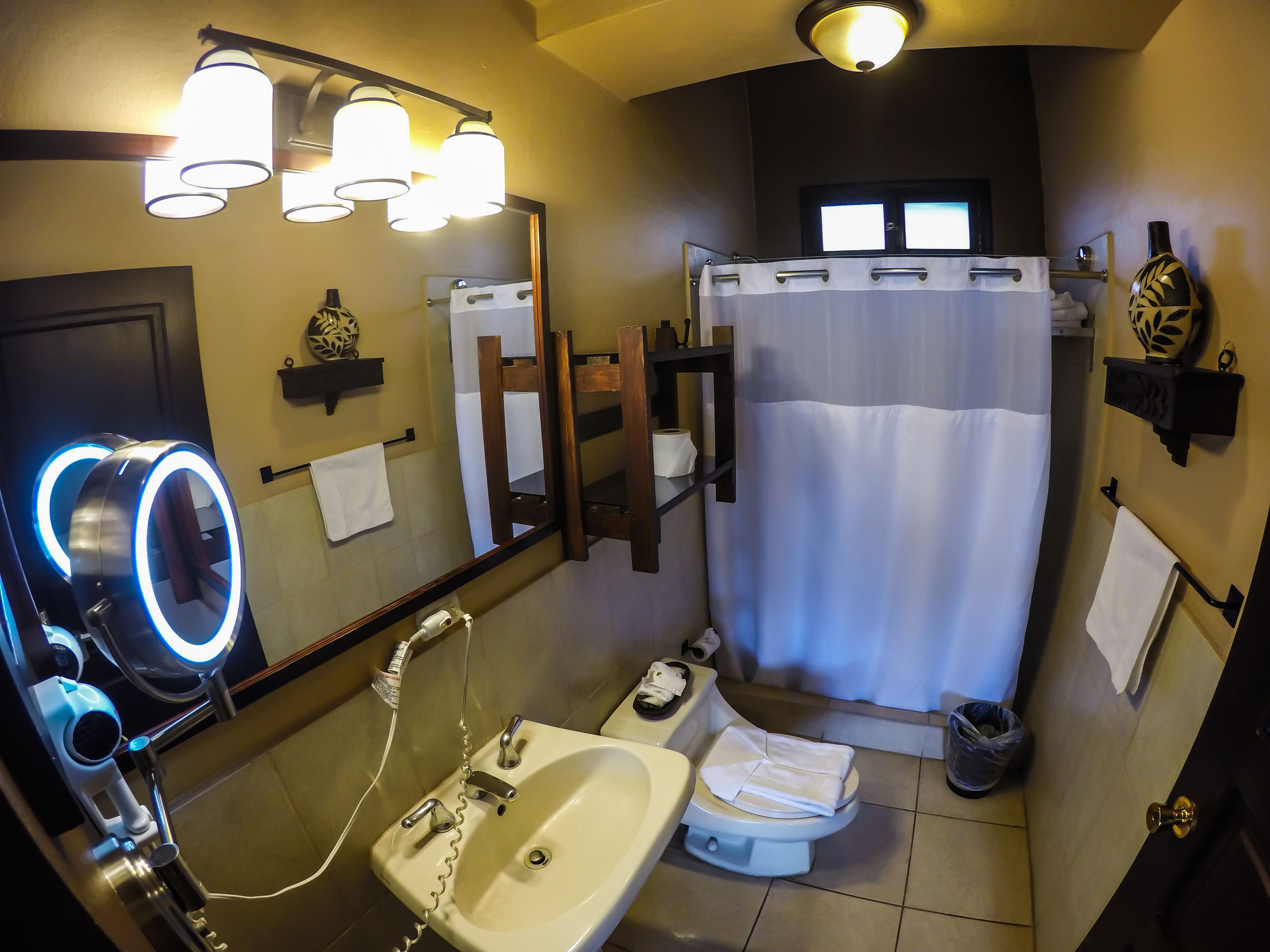 Une salle de bain équipée d’un lavabo, de toilettes et d’une douche. Il y a des lampes au-dessus du miroir et un porte-serviettes.