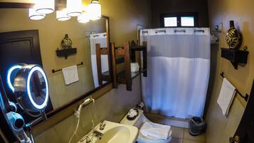 Une salle de bain équipée d’un lavabo, de toilettes et d’une douche. Il y a des lampes au-dessus du miroir et un porte-serviettes.