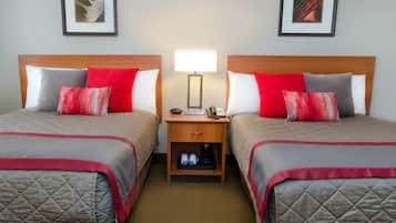 A hotel room with two beds, each with a red and white pillow, a bedside table with a lamp, and a drawer below.