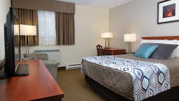 Une chambre d’hôtel comprenant un lit, deux tables de chevet, un bureau avec une lampe, une chaise et un téléviseur.