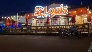 En St. Louis Bar & Grill med udendørs siddepladser og en motorcykel foran.