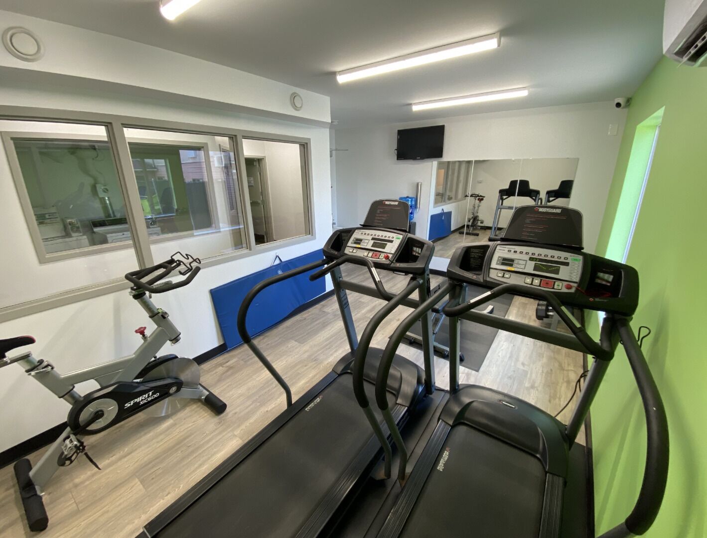 Un gimnasio con cintas de correr, bicicleta estática y un espejo.