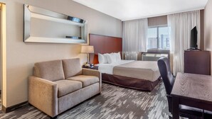 A hotel room with a bed, a sofa, a desk, a mirror, and a window with curtains. - Quality Inn Toronto Airport (Mississauga)