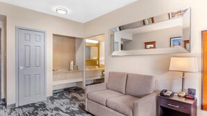 A hotel room with a grey door, a beige sofa, a bedside table with a lamp, a phone, and a mirror. - Quality Inn Toronto Airport (Mississauga)