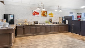 A modern kitchen with wooden cabinets, a central island, and a white brick wall with fruit-themed artwork. - Quality Inn Toronto Airport (Mississauga)