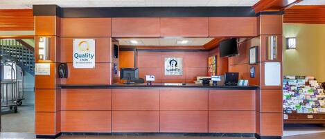 A reception desk at Quality Inn by Choice Hotels with a sign, a computer, and a telephone.