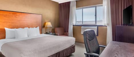 A hotel room with a large bed, a desk, a chair, a TV, and a window with curtains.