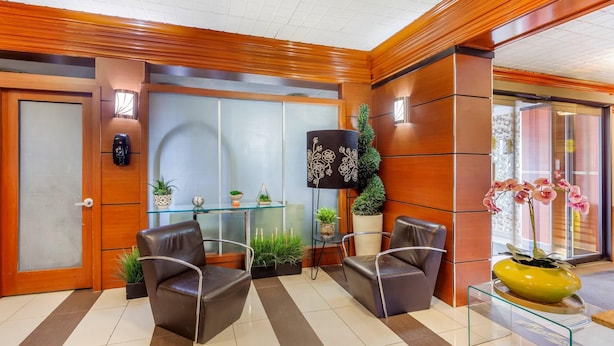 A reception area with a wooden reception desk, two leather chairs, a glass table, and a potted plant. - Quality Inn Toronto Airport (Mississauga)