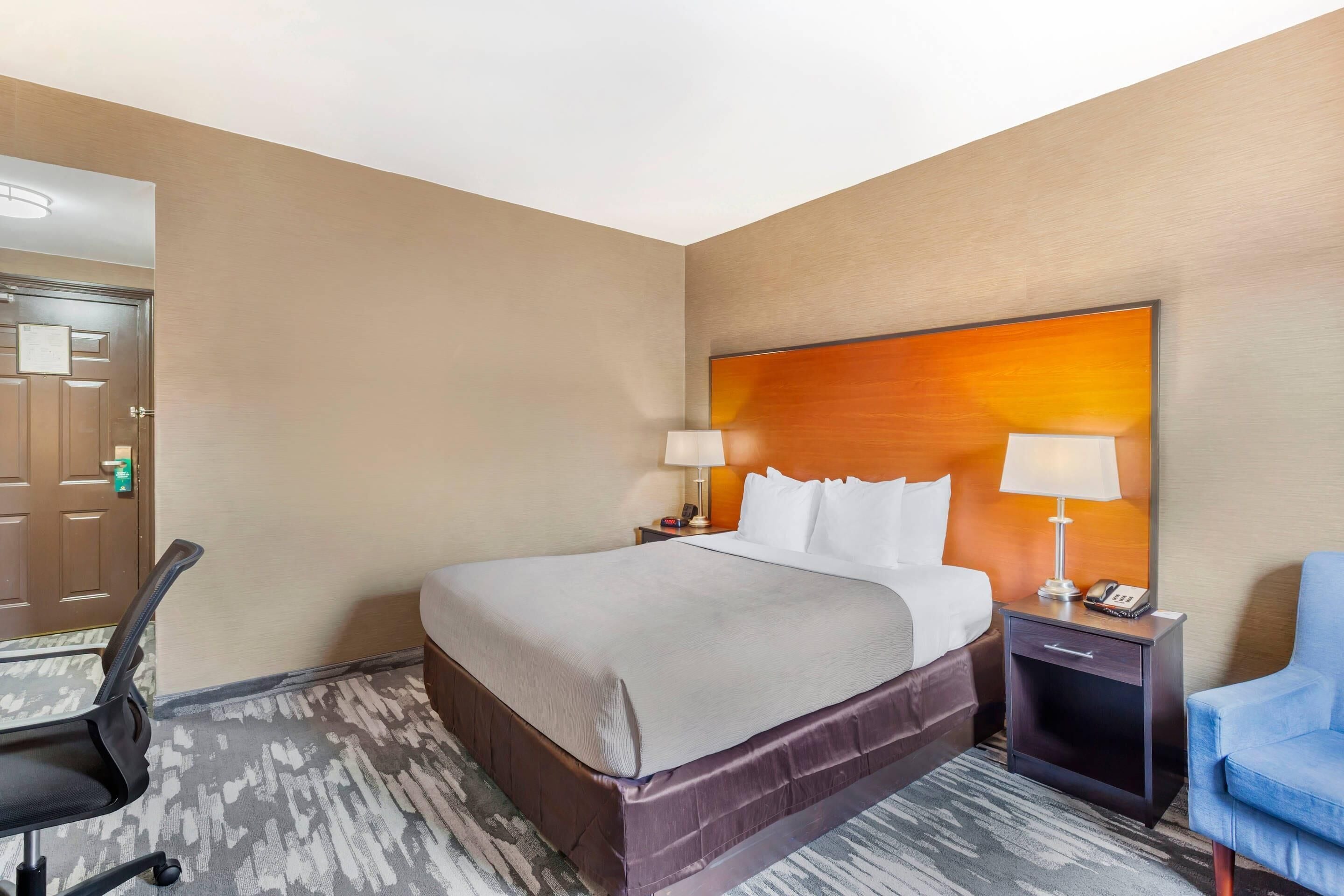 A hotel room with a large bed, two bedside tables, a chair, and a door.