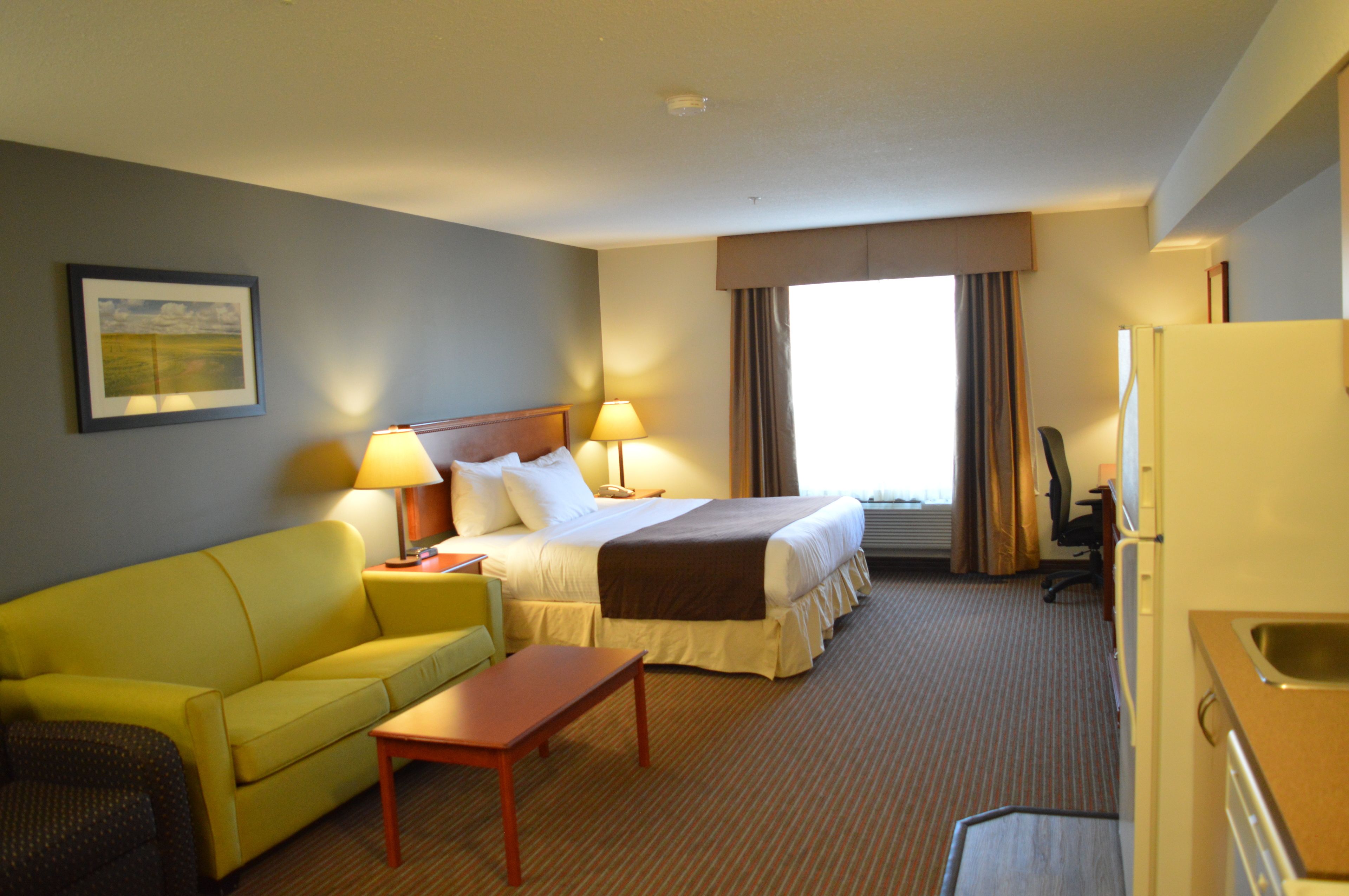 A hotel room with a bed, a yellow sofa, a wooden table, and a desk with a chair.