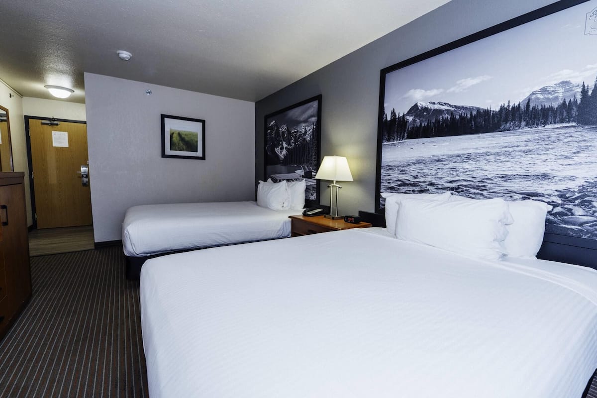 A hotel room with two beds, a nightstand with a lamp, a framed picture on the wall, and a door to the left.