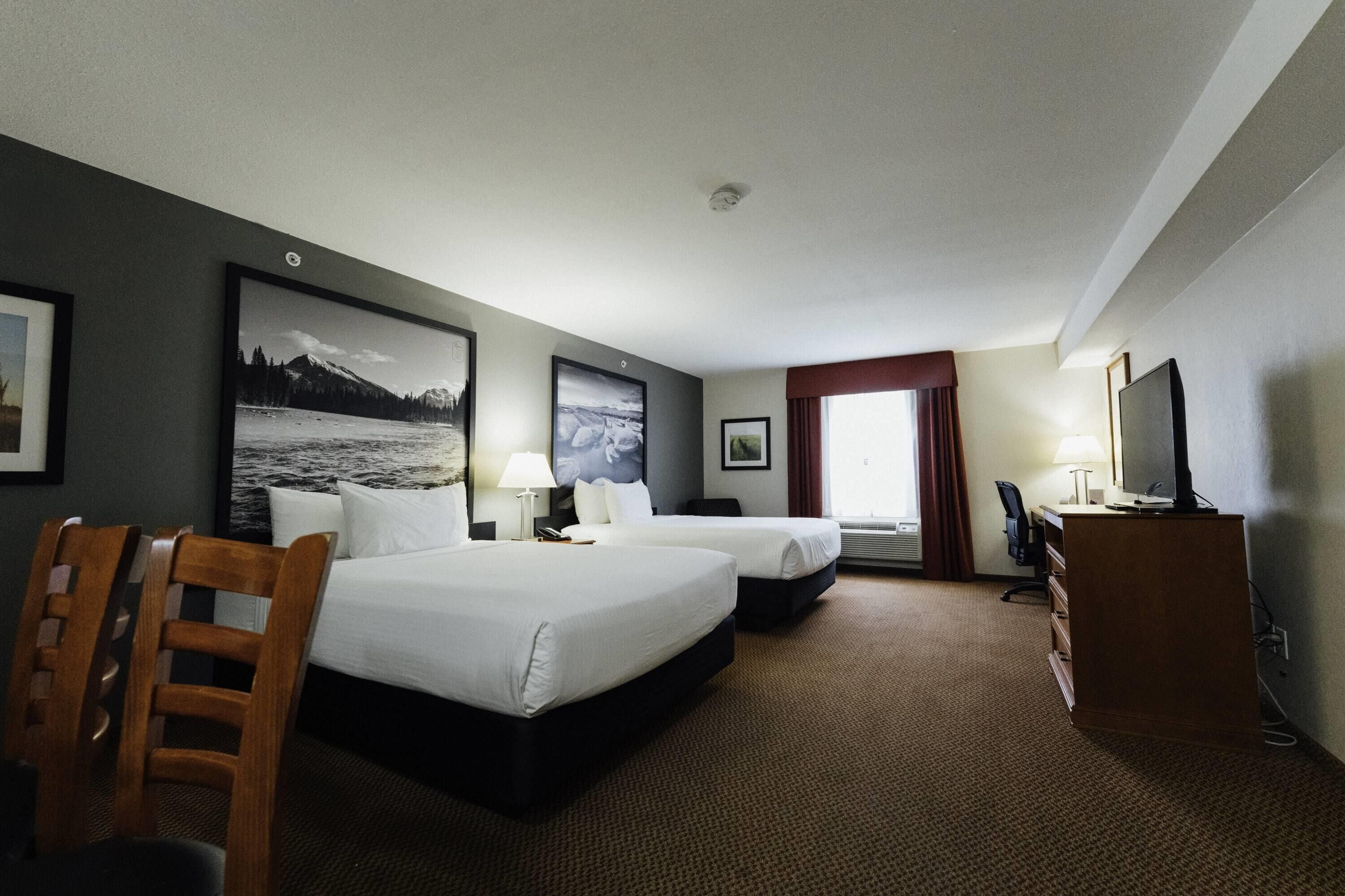 A hotel room with two beds, a desk, a chair, a TV, and a large window.
