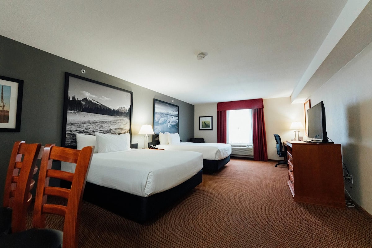 A hotel room with two beds, a desk, a TV, and a chair.