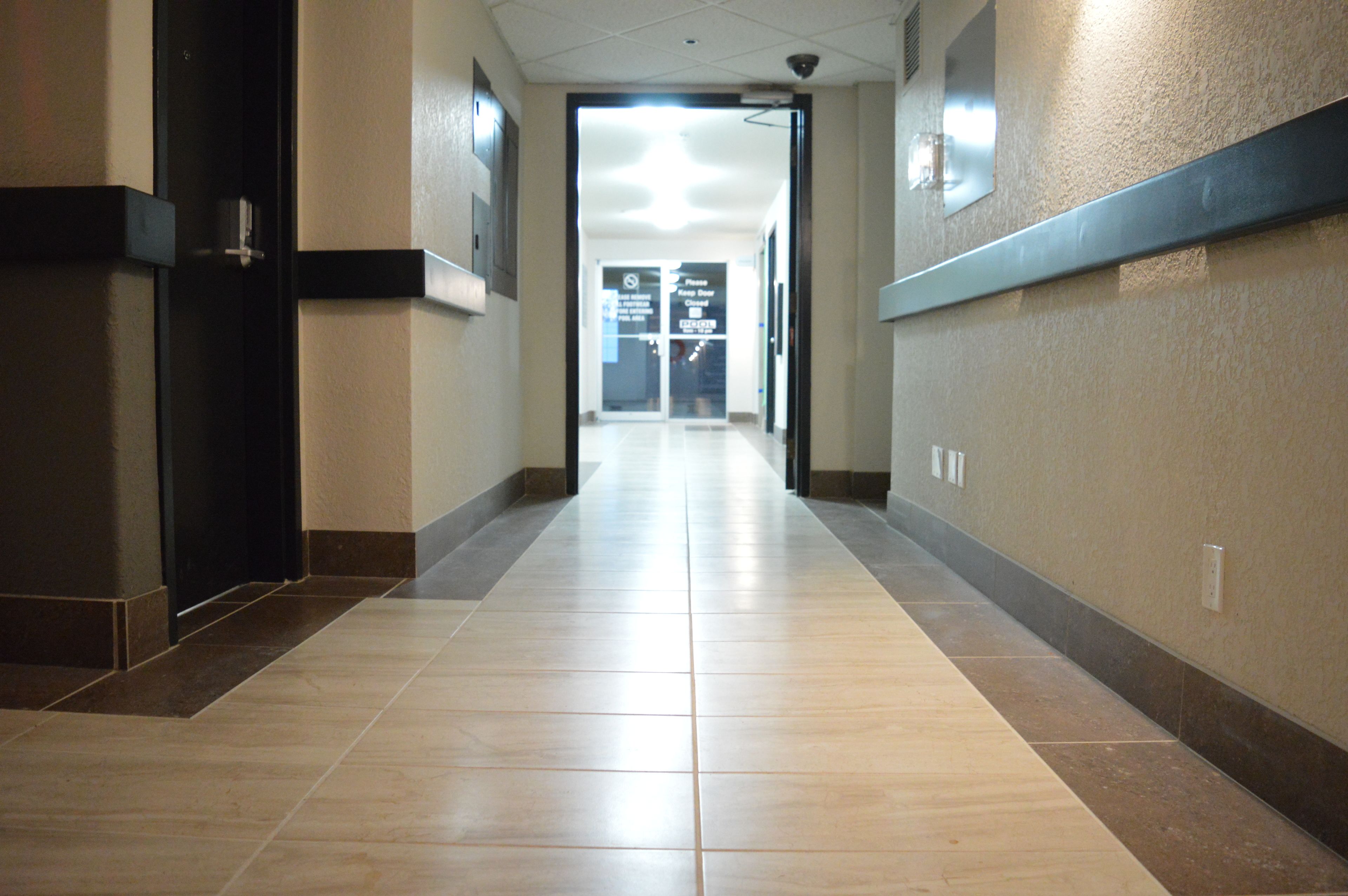Un long couloir étroit, dont le sol est recouvert de carreaux, qui mène à une porte au bout.
