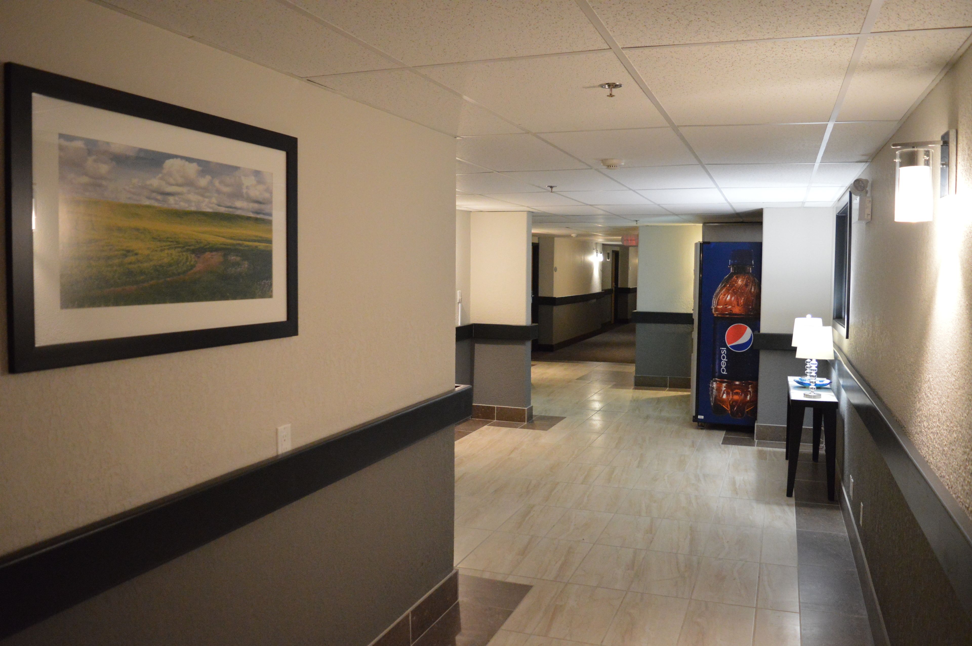 A hotel corridor with a framed landscape painting, a Pepsi vending machine, and a lamp on a small table.