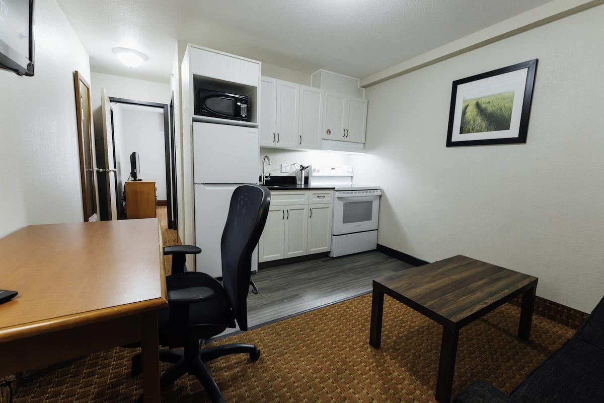 A compact kitchen with white cabinets, a microwave, and a stove. There's a wooden table and a black office chair.