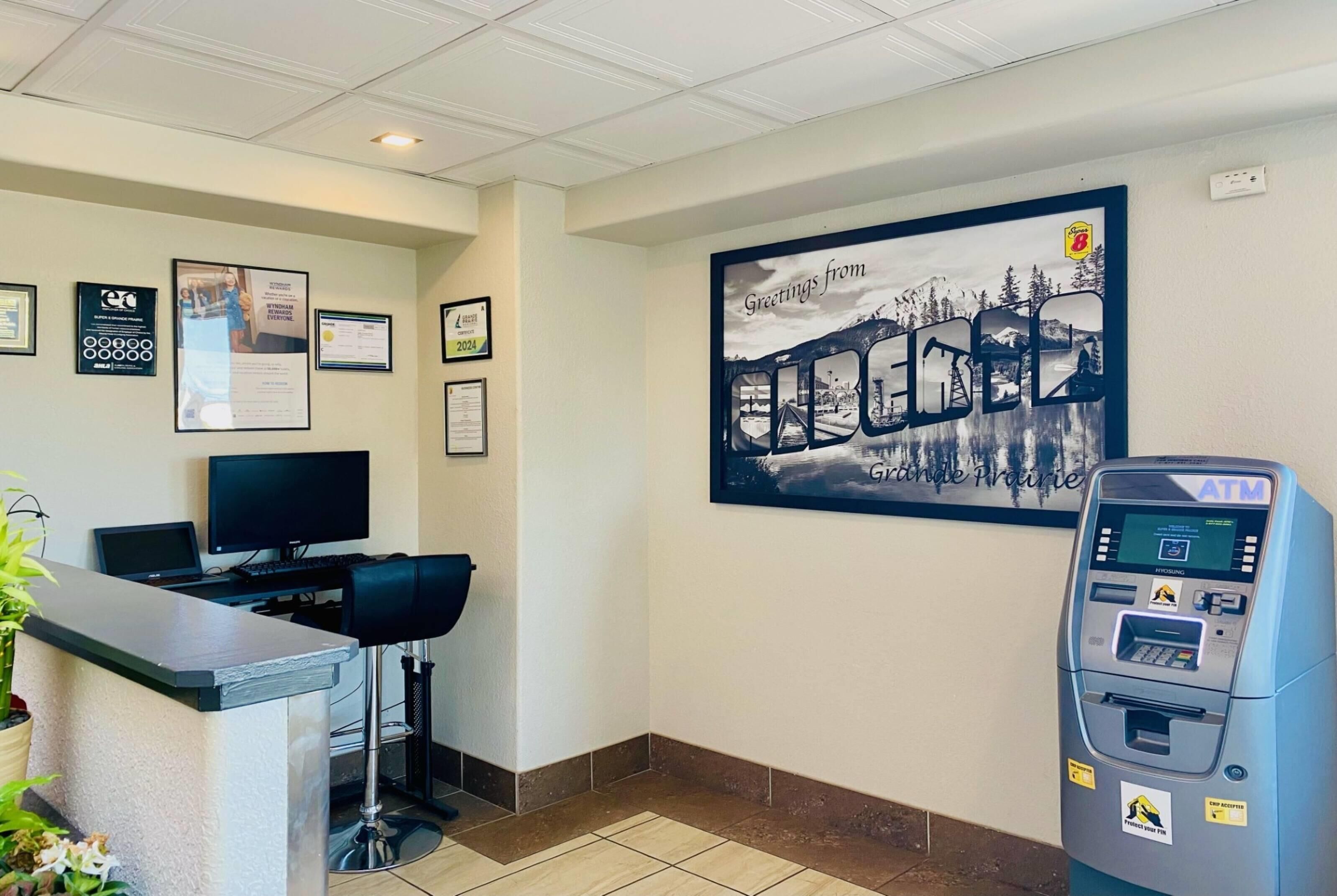 A reception area with a counter, a computer, framed certificates on the wall, and an ATM.