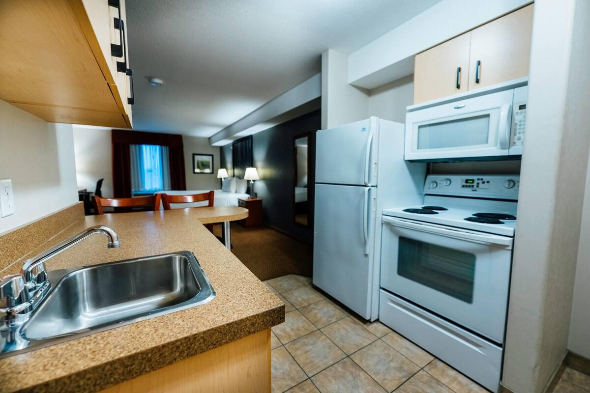 A modern kitchen with a granite countertop, stainless steel sink, white appliances, and a dining area with a table and chairs.