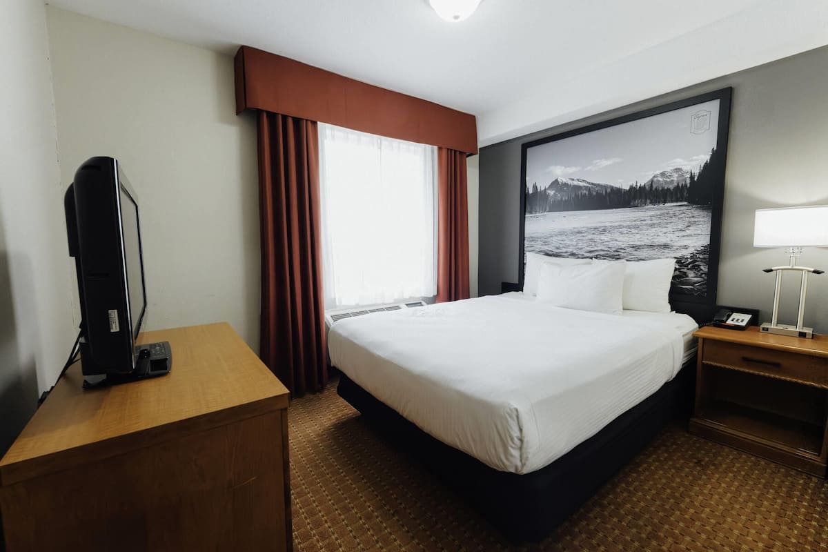 A hotel room with a large bed, a desk with a computer, a telephone, and a large window with curtains.
