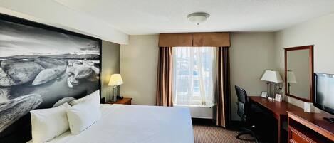 Habitación de hotel con una cama grande, un escritorio, una silla, un televisor, una ventana con cortinas y un cuadro en la pared.