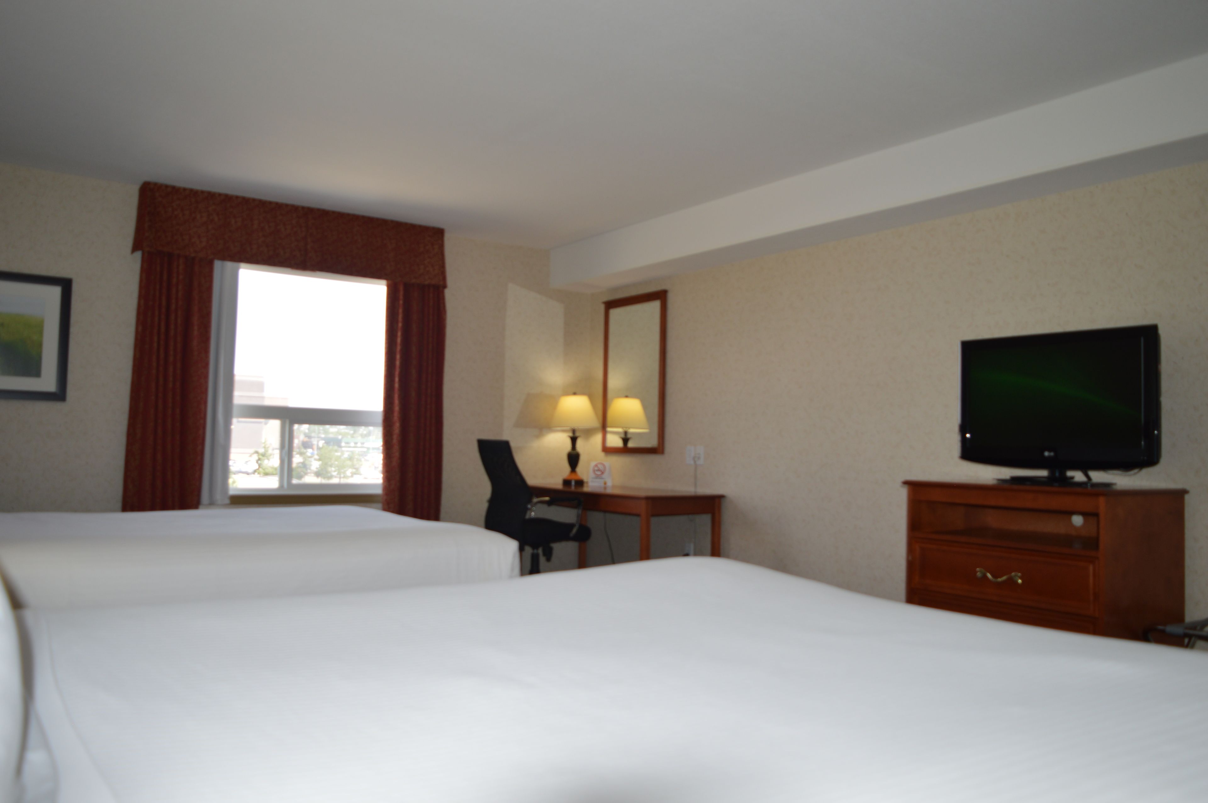 A hotel room with two beds, a desk with a chair, a television, and a window with curtains.