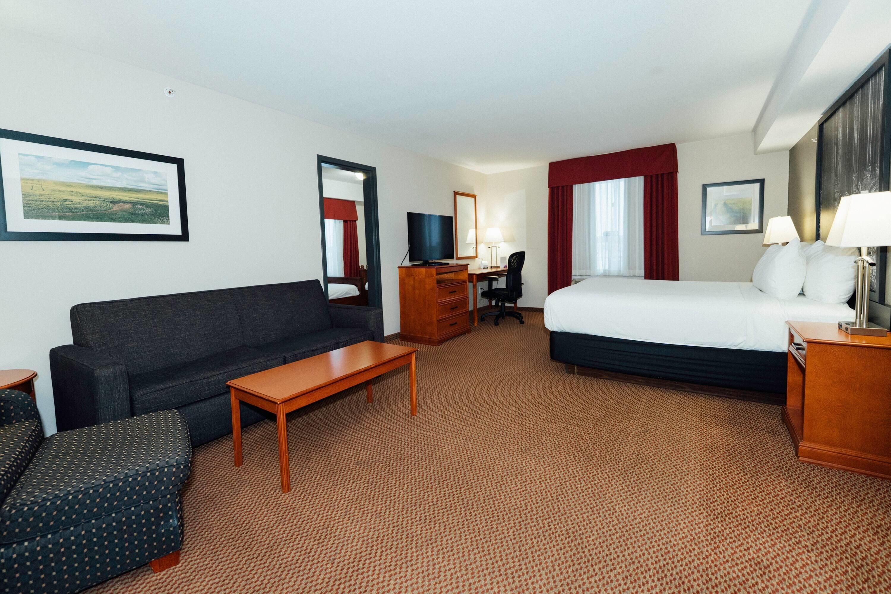A hotel room with a bed, a sofa, a desk, a TV, and a chair.