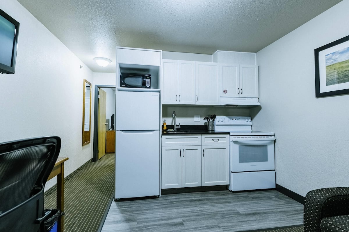 A compact kitchen with white cabinets, a microwave, a stove, and a refrigerator.